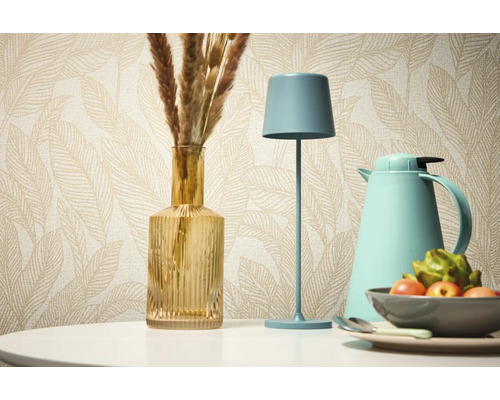 Dekoratives Stillleben mit Tischleuchte, Vase und Thermoskanne vor einer gemusterten Tapete.
