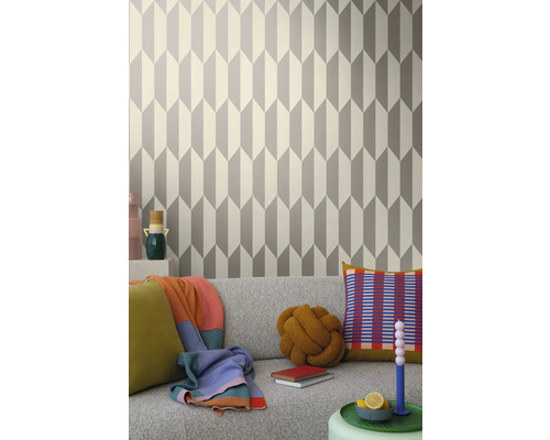 Wohnraum mit geometrischer Tapete in Grau und Weiß hinter einem grauen Sofa