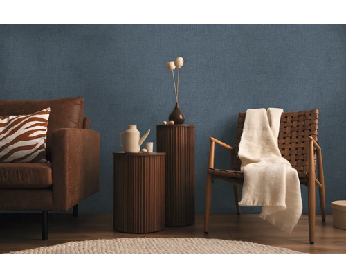 Wohnzimmer mit Sofa, Sessel, Beistelltischen und Dekor auf blau strukturierter Tapete