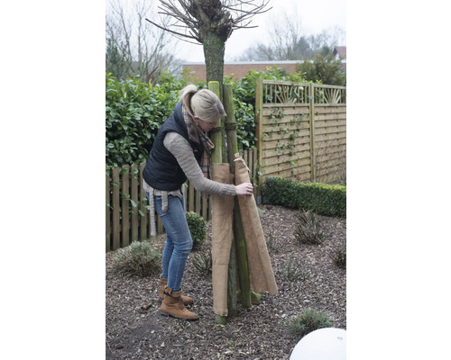 Eine Frau schützt einen Baum im Garten mit Jute vor Frost.