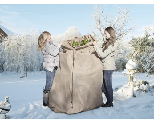 Zwei Personen verpacken Pflanzen in einen Winterschutzsack im verschneiten Garten.