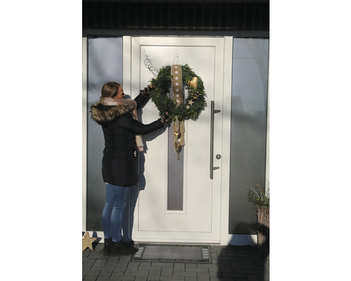 Frau befestigt einen geschmückten Adventskranz an einer Haustür.