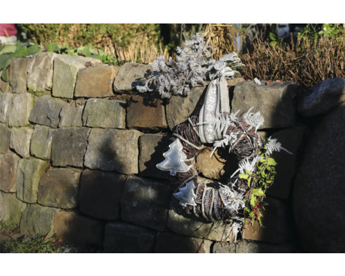 Dekorativer Adventskranz mit Schleife und Weihnachtsmotiven an einer Steinmauer