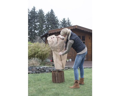 Frau schützt Pflanze mit Winterschutzhülle im Garten.