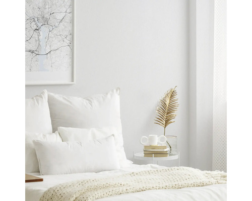 Helles Schlafzimmer mit Bett, Kissen, Beistelltisch und Dekorationsartikeln