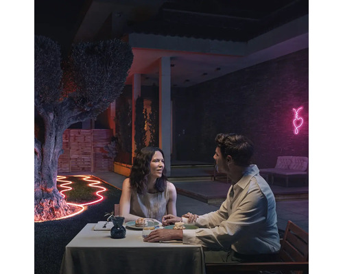 Ein Paar sitzt bei Nacht an einem Tisch im Garten, beleuchtet mit flexiblen Lichtbändern und einer Neonherzdekoration.