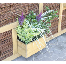 Holzkasten mit Pflanzen vor einem geflochtenen Zaun