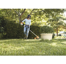 Eine Frau schneidet mit einem Rasentrimmer Gras in einem Garten.