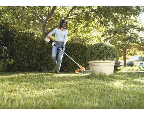 Eine Frau schneidet mit einem Rasentrimmer Gras in einem Garten.