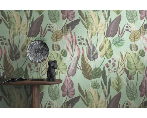 Detailaufnahme einer Wand mit einer Tapete mit Blättermuster, einem Tisch mit einem Buch, einer Dekofigur und einem Teller.