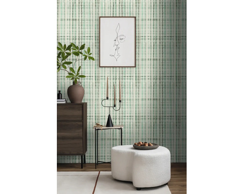 Wohnraum mit gemusterter Tapete, Kommode, Beistelltisch und Ottomane.