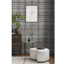 Wohnraum mit gemusterter Tapete, Kommode, Beistelltisch, Kerzenständer und Hocker.