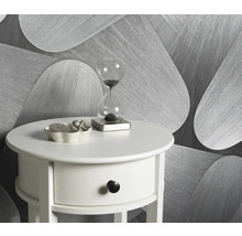 Szene mit einem weißen Beistelltisch, einer Sanduhr und einer Dekoschale vor einer gemusterten Tapete