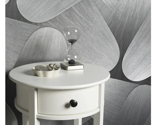 Szene mit einem weißen Beistelltisch, einer Sanduhr und einer Dekoschale vor einer gemusterten Tapete