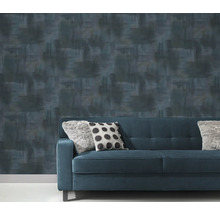 Gemusterte Tapete hinter einem blauen Sofa mit Kissen