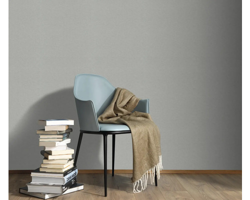 Szene mit einem Stuhl, einer Decke und einem Bücherstapel vor einer grauen Wand.