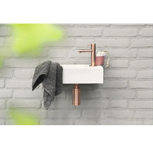 Kleines Waschbecken mit Armatur, Handtuch und Seifenspender an einer Ziegelwand