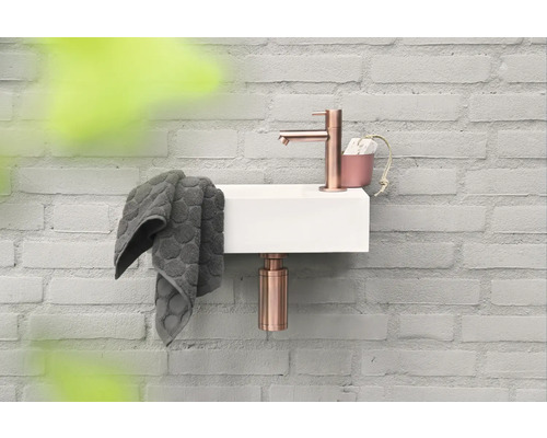 Kleines Waschbecken mit Armatur, Handtuch und Seifenspender an einer Ziegelwand