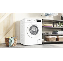 Weiße Waschmaschine neben einem Regal und einem Wäschekorb.