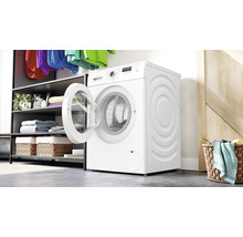 Weiße Bosch Waschmaschine mit offener Tür in einem Wäscheraum mit Regal