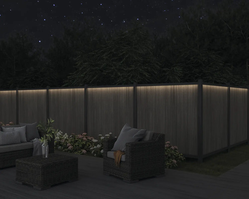 Eine Holzterrasse mit Lounge-Möbeln und einem beleuchteten Holzzaun bei Nacht.