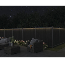 Gartenmöbel auf einer Terrasse mit beleuchtetem Zaun im Dunkeln