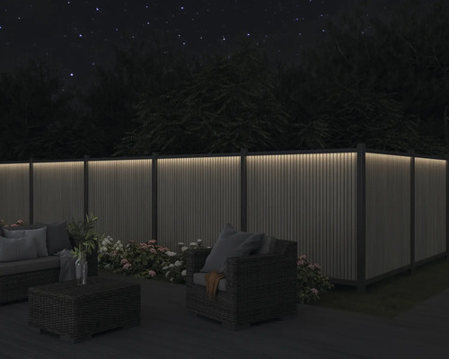 Gartenmöbel-Set auf einer Terrasse mit beleuchtetem Holzzaun bei Nacht