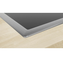 Detailansicht eines Kochfelds aus Glaskeramik mit Edelstahlrahmen, eingebaut in eine Holzarbeitsplatte.