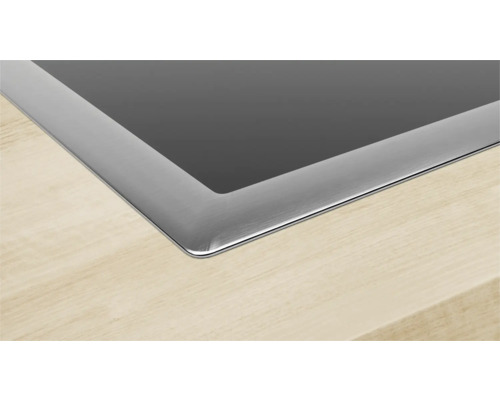 Detailansicht eines Kochfelds aus Glaskeramik mit Edelstahlrahmen, eingebaut in eine Holzarbeitsplatte.