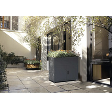 Szene mit einem grauen Pflanzkasten mit Türen und Pflanzen auf einer Terrasse.