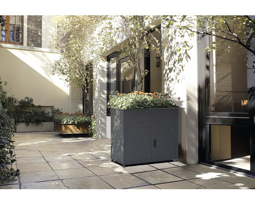 Szene mit einem grauen Pflanzkasten mit Türen und Pflanzen auf einer Terrasse.