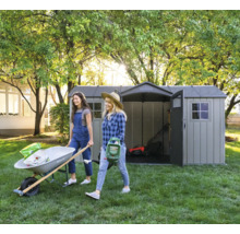 Gartenszene mit zwei Frauen, die eine Schubkarre und einen Rasensprenger tragen, im Hintergrund ein Gartenschuppen