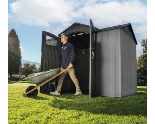 Mann schiebt Schubkarre aus einem Geräteschuppen im Garten
