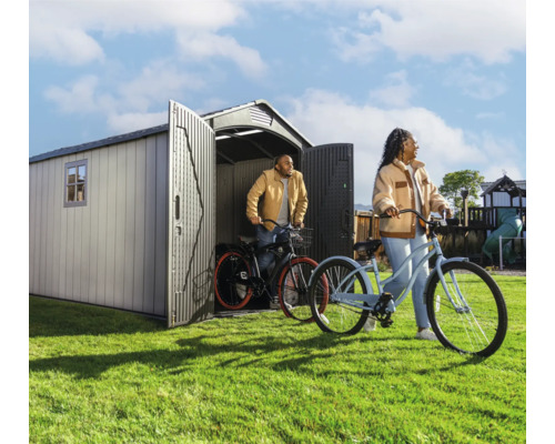 Gartenszene mit Gerätehaus und zwei Personen mit Fahrrädern auf dem Rasen