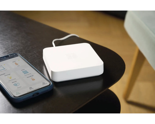 Intelligentes Haus System mit Smartphone-App und Zentraleinheit auf einem Tisch.