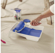 Eine Person befüllt eine Farbwanne mit einem Farbroller mit Farbe zum Malen.