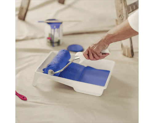 Eine Person befüllt eine Farbwanne mit einem Farbroller mit Farbe zum Malen.