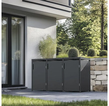 Drei Mülltonnenboxen vor einem Haus mit Pflanzen darauf und neben einer Steinmauer.