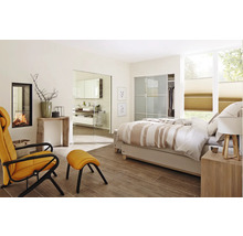 Helles Schlafzimmer mit Kamin, Sessel und Badezimmerzugang durch eine Glastür