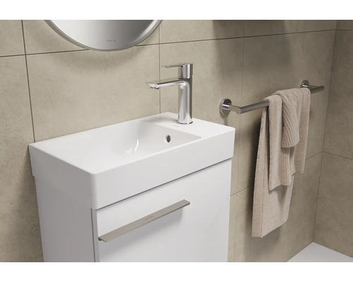 Waschtisch mit Armatur, Handtuch und Spiegel in einem Badezimmer.