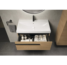 Waschtischunterschrank mit offenem Schubfach, darin Handtücher und Pflegeprodukte. Über dem Waschbecken hängt ein Spiegel.