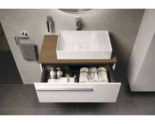 Modernes Badezimmer mit weißem Aufsatzwaschbecken auf Holzplatte und offenem Schubladenelement gefüllt mit Handtüchern und Pflegeprodukten.
