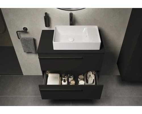 Badezimmer mit schwarzem Waschtischunterschrank, weißem Aufsatzwaschbecken und geöffneter Schublade mit Badutensilien
