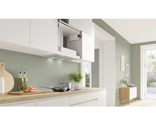 Helle Küche mit Dunstabzugshaube unter einem weißen Hängeschrank, Kochfeld, Spüle und Kochutensilien auf der Arbeitsfläche.