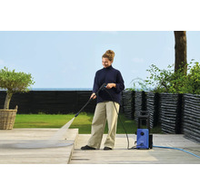 Eine Frau reinigt eine Holzterrasse mit einem Hochdruckreiniger.