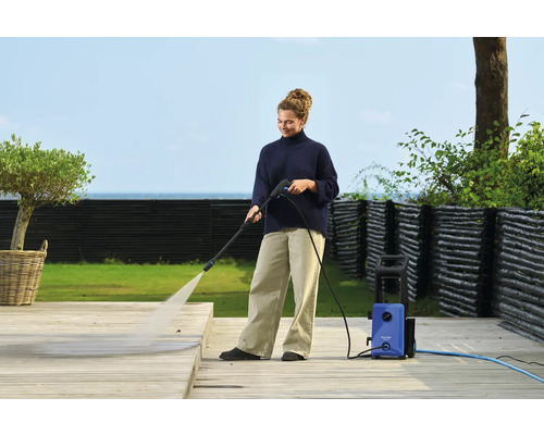 Eine Frau reinigt eine Holzterrasse mit einem Hochdruckreiniger.
