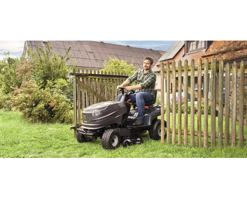 Ein Mann fährt einen Rasentraktor auf einer Rasenfläche neben einem Holzzaun.