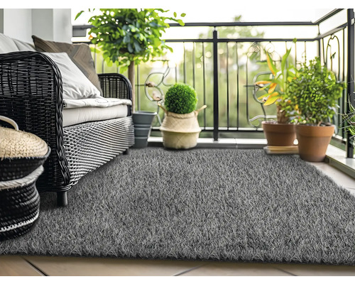 Balkonszene mit Rattansofa, Pflanzen und grauem Kunstrasen