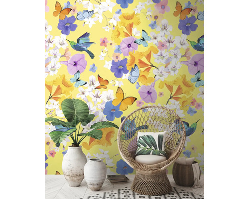 Dekoratives Interieur mit gelber Tapete, verziert mit Blumen, Schmetterlingen und Vögeln, ergänzt durch Korbsessel und Zimmerpflanzen