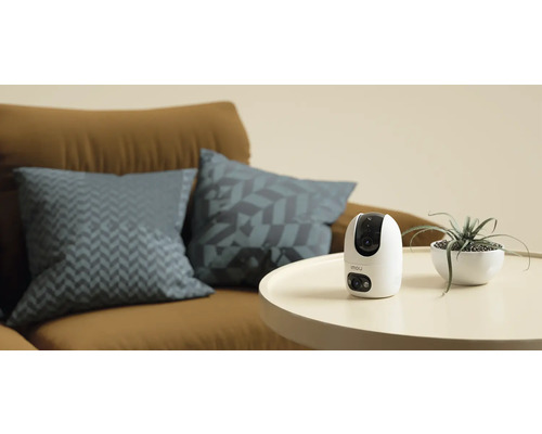 Imou Überwachungskamera auf einem Tisch neben einer Zimmerpflanze und einem Sofa
